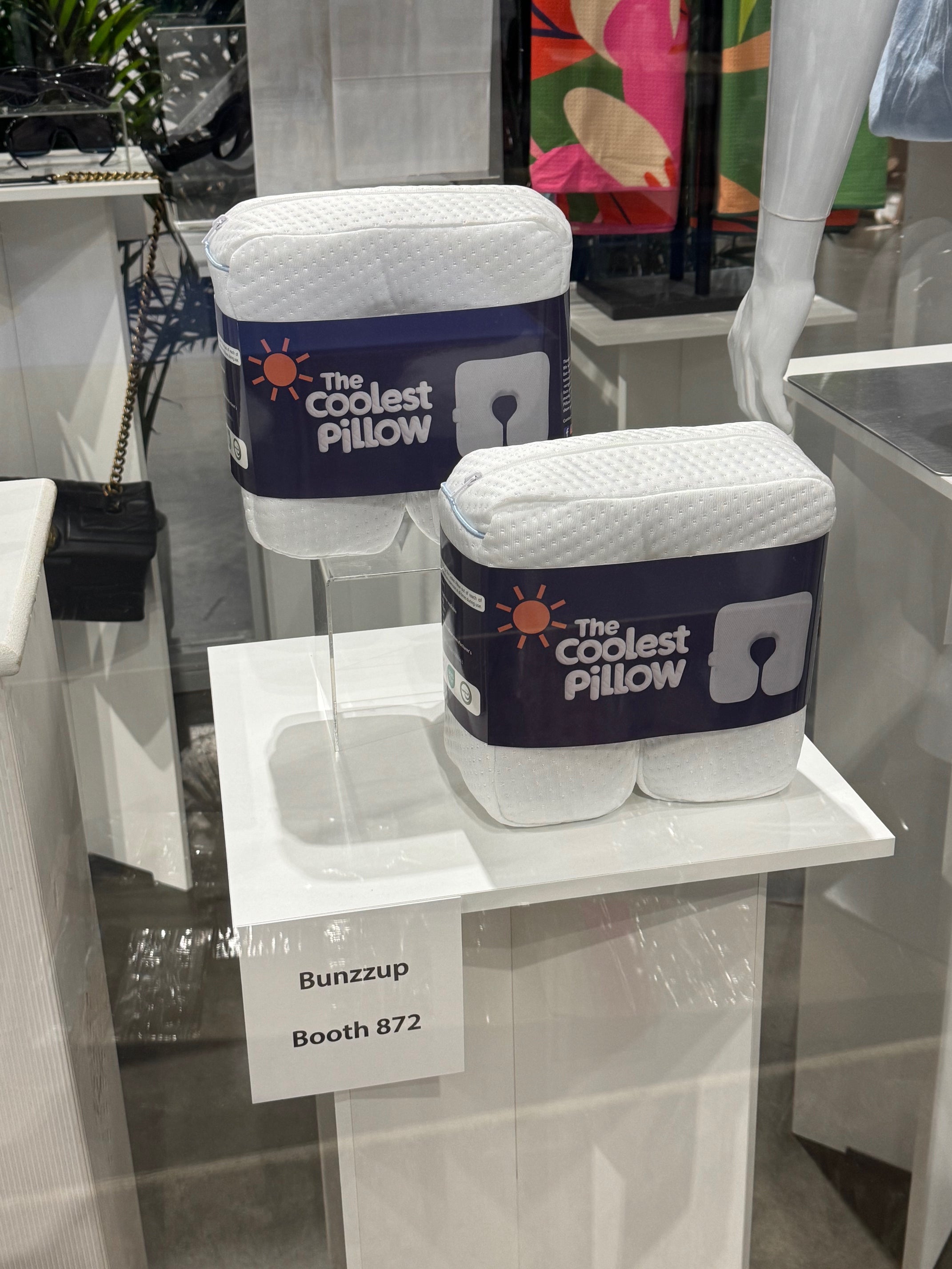 The Coolest Pillow by Bunzzup, a cooling beach pillow, showcased on a stand at Booth 872, for neck support.